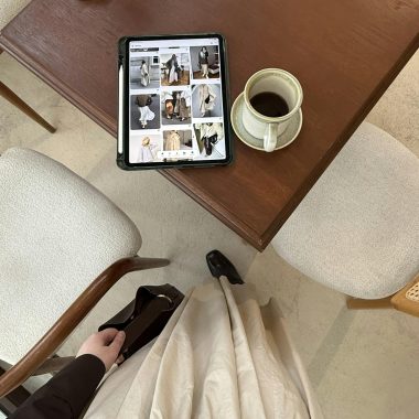 Top-down view of person browsing fashion on tablet with coffee at a cozy cafe table.